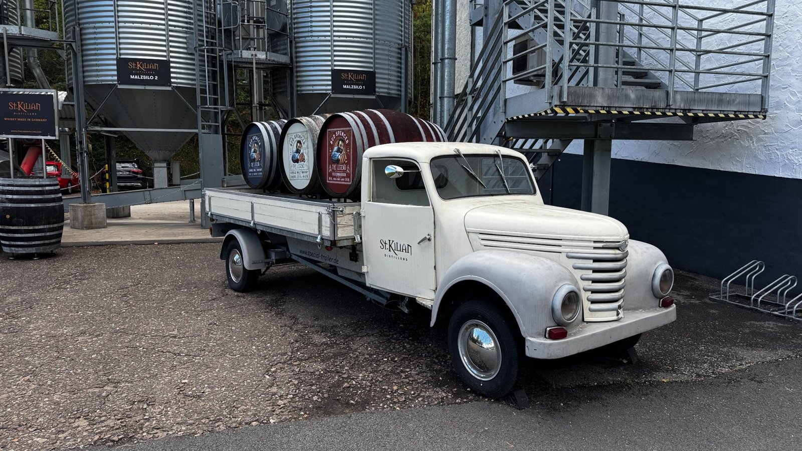 Weißer Oldtimer-Lastwagen mit Bud-Spencer-Fässern vor den Malzsilos